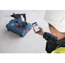 Bosch Akku-Bohrhammer auf einem Werkzeugkoffer, ein Arbeiter mit Schutzhelm betrachtet ein Mobiltelefon