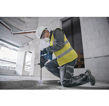 Ein Bauarbeiter kniet und benutzt einen Bohrhammer auf einer Baustelle.