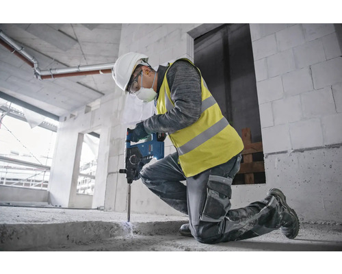 Ein Bauarbeiter kniet und benutzt einen Bohrhammer auf einer Baustelle.