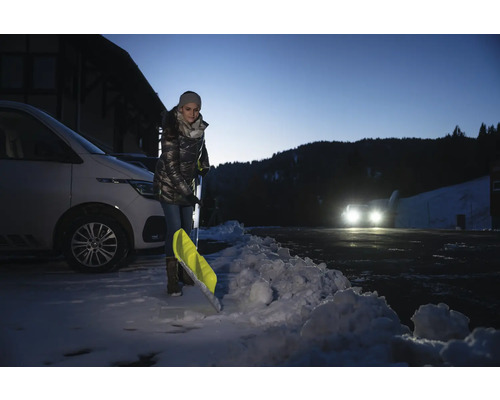 Frau schaufelt Schnee mit einer Schneeschaufel neben einem Auto.