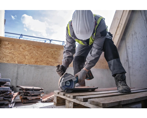 Ein Bauarbeiter schneidet mit einer Trennscheibe Dachziegel auf einer Palette