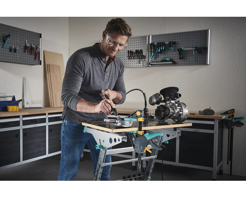Ein Mann arbeitet mit einem Multifunktionswerkzeug an einem Werkstück auf einem Werktisch von Wolfcraft in einer Werkstatt.