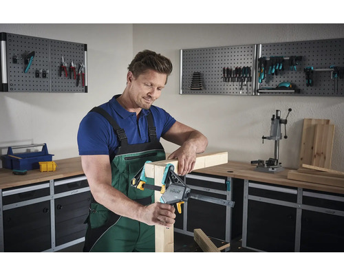 Mann verwendet eine Einhandzwinge in einer Werkstatt zum Fixieren von Holz.