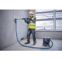Handwerker bohrt mit Bohrhammer ein Loch in eine Betonwand mit Staubabsaugung