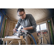 Ein Mann sägt ein Holzbrett mit einer Bosch Kreissäge in einem Holzhaus.