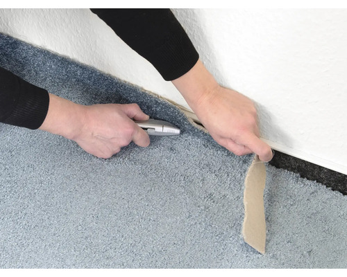 Zuschneiden eines Teppichs mit einem Cuttermesser an einer Wand entlang