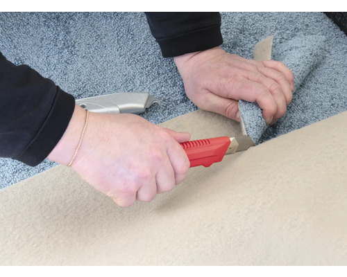 Zwei Hände schneiden einen Teppich mit einem Teppichmesser.