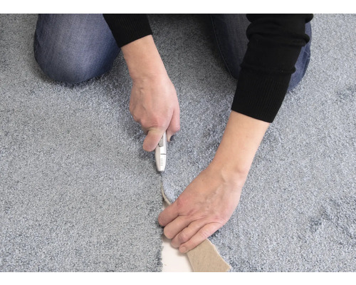 Eine Person schneidet mit einem Teppichmesser einen Teppich zu.