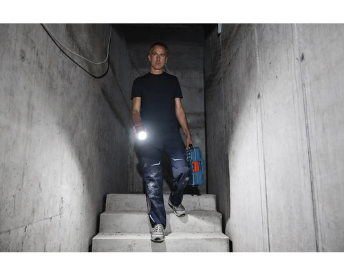 Mann geht mit Taschenlampe und Werkzeugkoffer eine Betontreppe hinunter