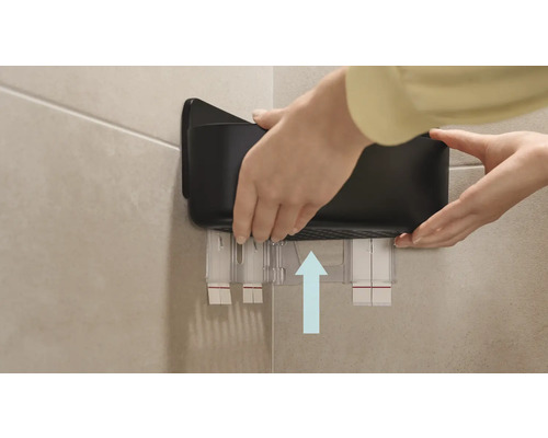 Eine Person befestigt ein schwarzes Badezimmerregal an der Wand.