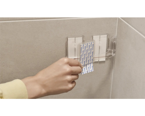 Person befestigt Klebestreifen an einer Halterung im Badezimmer.