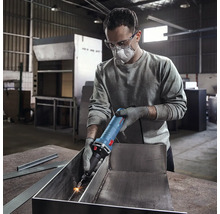 Mann mit Schutzbrille und Mundschutz verwendet einen Geradschleifer zur Metallbearbeitung in einer Werkstatt.