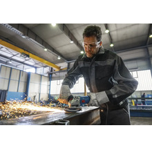 Ein Mann arbeitet mit einem Winkelschleifer an Metall und trägt dabei Schutzkleidung.