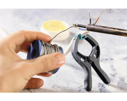 Lötzinnrolle in der Hand, Lötarbeiten an einem Kabel mit einer Klemme fixiert