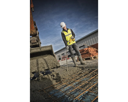 Ein Bauarbeiter verdichtet Beton mit einem Betonrüttler, während ein Bagger Beton ablädt.