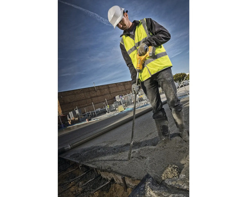 Ein Bauarbeiter verdichtet Beton mit einem Betonrüttler auf einer Baustelle.