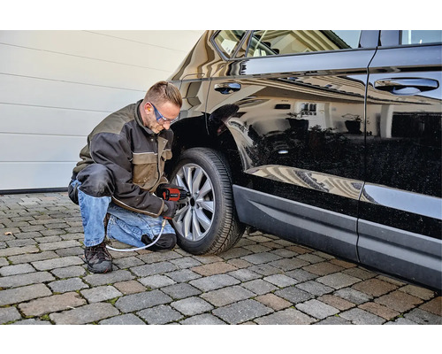 Mann wechselt mit einem Akku-Schlagschrauber einen Reifen an einem Auto.
