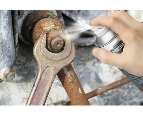 Eine Person sprüht Rostlöser auf eine Mutter, die mit einem Schraubenschlüssel gehalten wird.
