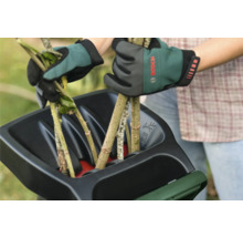 Zwei Hände mit Gartenhandschuhen befüllen einen Häcksler mit Ästen.