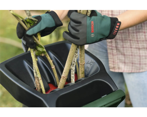 Zwei Hände mit Gartenhandschuhen befüllen einen Häcksler mit Ästen.