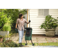 Frau bedient einen Häcksler im Garten mit Gartengeräten und Gartenabfällen