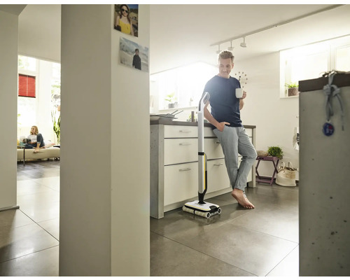 Ein Mann lehnt mit einer Tasse in der Hand an einer Küchentheke neben einem elektrischen Wischmopp.