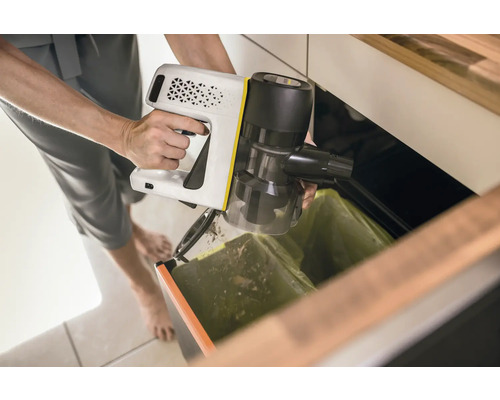 Eine Person entleert einen Akku-Staubsauger über einem Mülleimer.