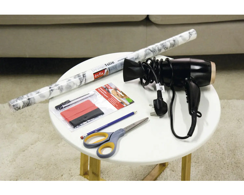 Dekorfolie, Rakel, Cutter, Fön, Bleistift und Schere auf einem Tisch