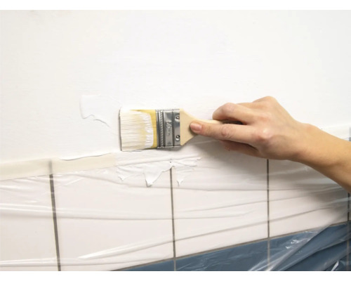 Hand streicht Wand mit Pinsel und Farbe in Badezimmer