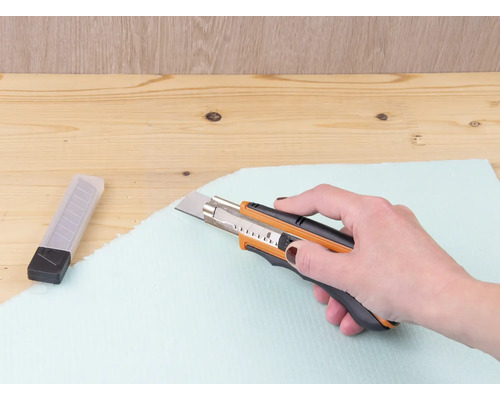 Eine Hand schneidet mit einem Teppichmesser eine Dämmplatte.