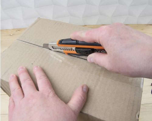 Eine Person öffnet einen Karton mit einem Cuttermesser.