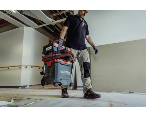 Handwerker trägt Metabo Industriesauger mit Zubehör durch einen Raum.