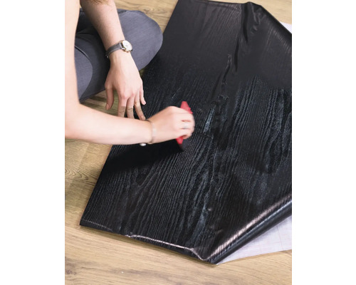 Person verarbeitet eine selbstklebende Möbelfolie in Holzoptik mit einem Rakel.