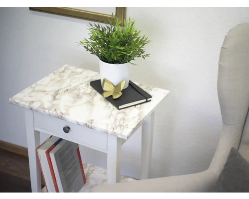 Dekoratives Arrangement auf einem weißen Beistelltisch mit Marmoroptik, bestehend aus einer Pflanze im Topf, einem Notizbuch und einer Dekofigur.