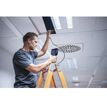 Ein Mann inspiziert eine Decke mit einer Inspektionskamera von einer Leiter aus