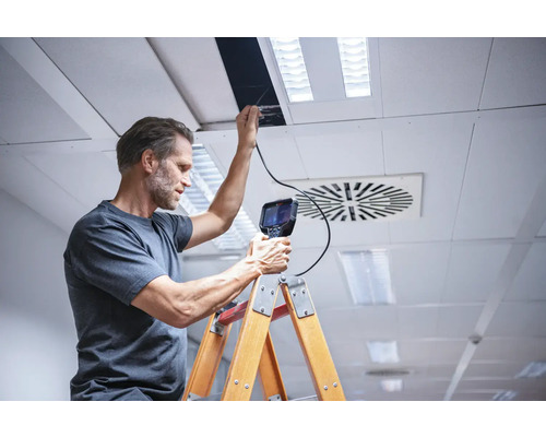 Ein Mann inspiziert eine Decke mit einer Inspektionskamera von einer Leiter aus