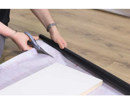 Zuschneiden von Dekorfolie mit einer Schere zum Aufbringen auf ein Möbelstück