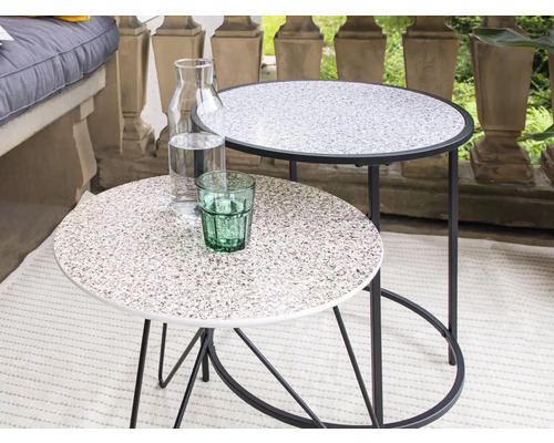 Zwei runde Beistelltische mit Tischplatten in Steinoptik, eine Wasserflasche und ein Trinkglas stehen auf einem Balkon.