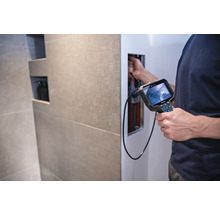 Ein Mann verwendet eine Inspektionskamera von Bosch, um Rohre in einer Wand zu untersuchen.