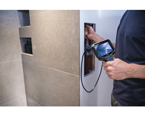 Ein Mann verwendet eine Inspektionskamera von Bosch, um Rohre in einer Wand zu untersuchen.