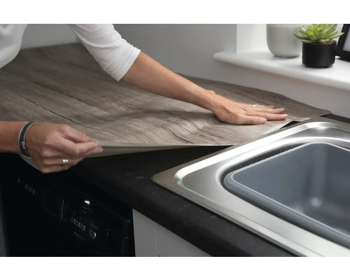 Person bringt selbstklebende Folie in Holzoptik auf einer Küchentheke an