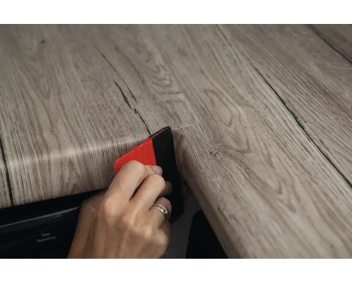 Eine Person bringt eine Holzdekorfolie mit einem Rakel an