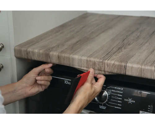 Person bringt eine selbstklebende Folie in Holzoptik an einer Arbeitsplatte an