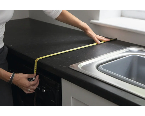 Eine Person misst eine Küchentheke mit einem Maßband.