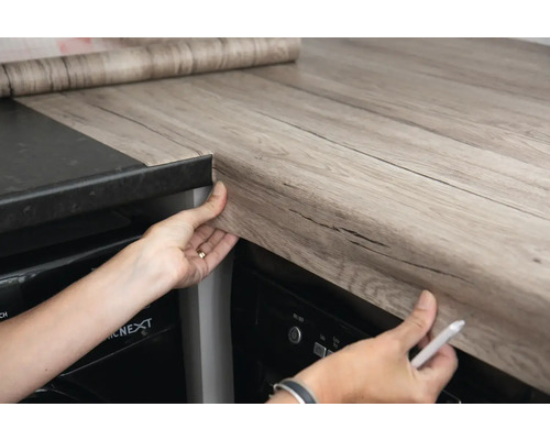 Küchenszene mit einer Person, die eine selbstklebende Folie auf einer Küchentheke anbringt.