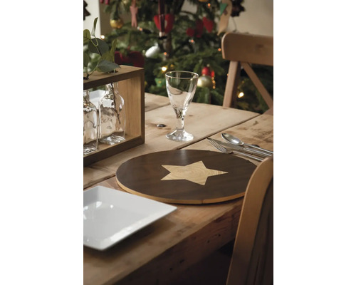 Festlich gedeckter Holztisch mit Geschirr, Besteck und Dekoration vor einem Weihnachtsbaum.