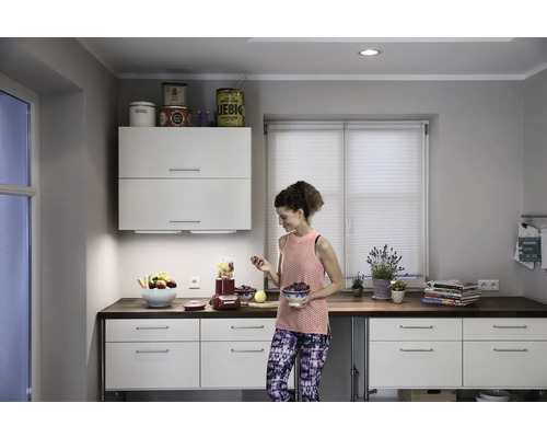 Helle Küche mit weißen Schränken, dunkler Arbeitsplatte und einer Frau, die Obst in einer Schüssel hält.