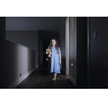 Mädchen mit Teddybär auf einem dunklen Flur mit Wandleuchten