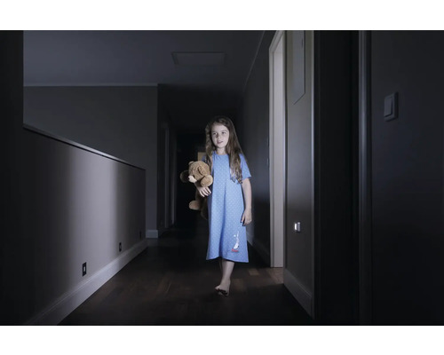 Mädchen mit Teddybär auf einem dunklen Flur mit Wandleuchten
