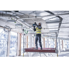 Ein Bauarbeiter steht auf einem Gerüst und befestigt eine Deckeninstallation.